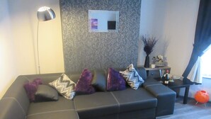 A modern living room with a sectional sofa, a floor lamp, a small table with a vase, and a decorative mirror on the wall. - Magdala House (Liverpool)