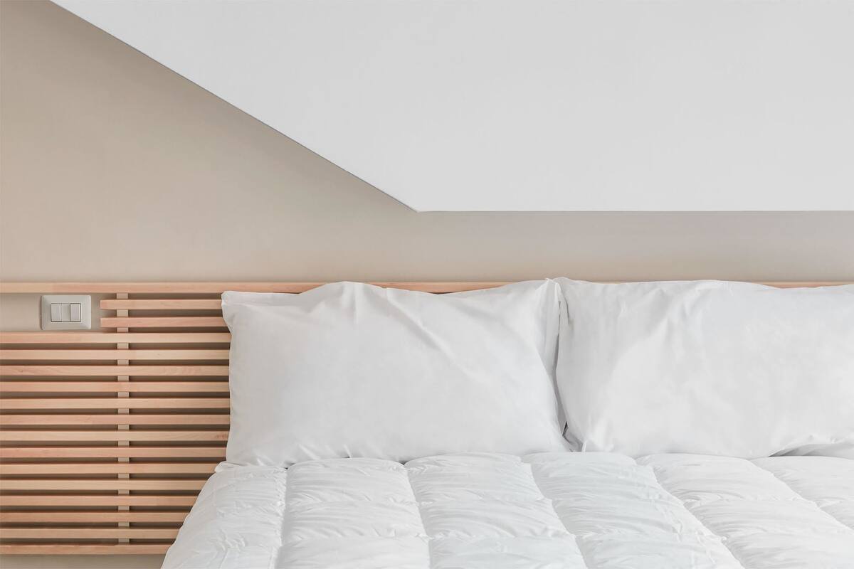 Un dormitorio con cabecera de listones, ropa de cama blanca e interruptor de luz a la vista.
