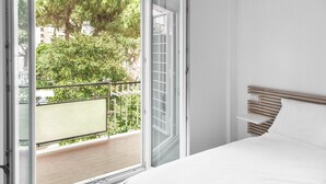 A bedroom with a bed, a wooden headboard, a balcony with a railing, and a view of trees and buildings outside. - B&B Jonio Roma (Rome)