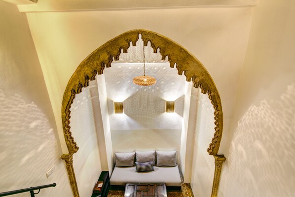A cozy seating area with a cushioned bench, a decorative hanging light, and an ornate archway. - Riad Amaris (Rabat)