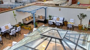 An outdoor patio area with seating arrangements, potted plants, and a glass roof structure. - Riad Amaris (Rabat)