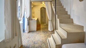 A staircase leading to a second-floor sleeping area with a bed, a small bathroom with a sink and towel rack, and a herringbone-patterned floor. - Riad Amaris (Rabat)