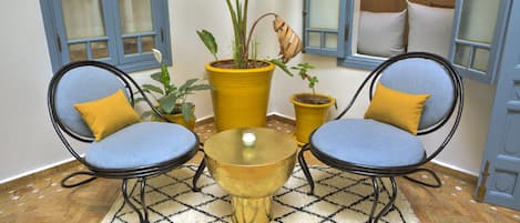 A room with two blue chairs, a small round table, and a yellow potted plant.