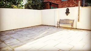 Une terrasse avec un banc, un mur blanc et un bâtiment en briques en arrière-plan.