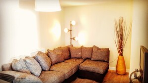 Un salon chaleureux avec un canapé d’angle, une lampe sur pied et un vase décoré de branches.