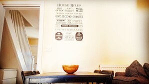 Un coin repas avec une table en bois, des chaises et un bol posé sur la table. On peut voir un mur orné de différentes phrases motivantes.