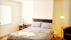 Une chambre à coucher bien rangée, avec un lit, une table de chevet, une lampe et une fenêtre.