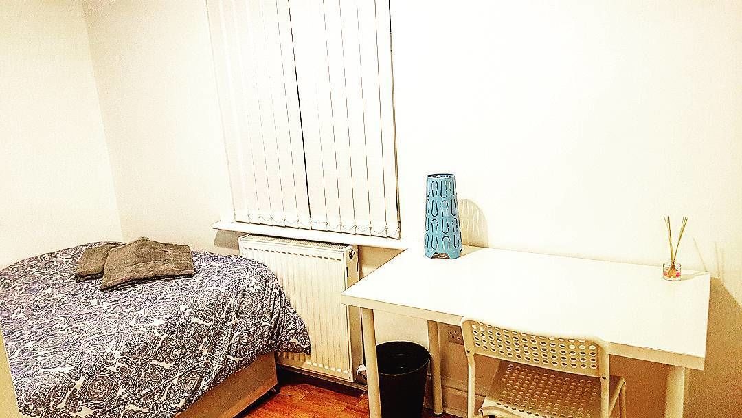 A bedroom with a bed, a desk, a radiator, and a window with blinds.
