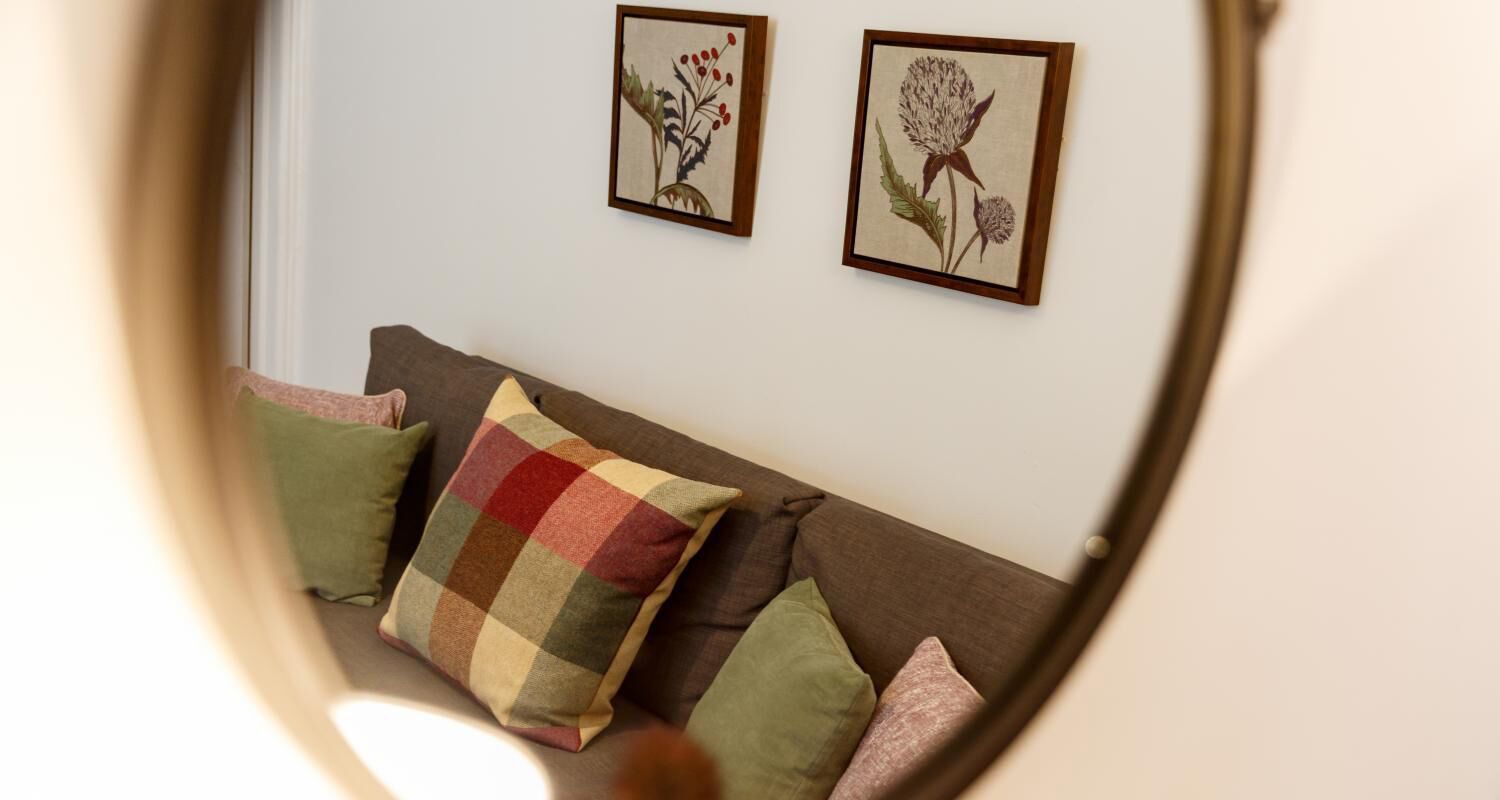 Une pièce avec un canapé marron, des coussins verts et multicolores, et deux reproductions botaniques encadrées accrochées au mur.