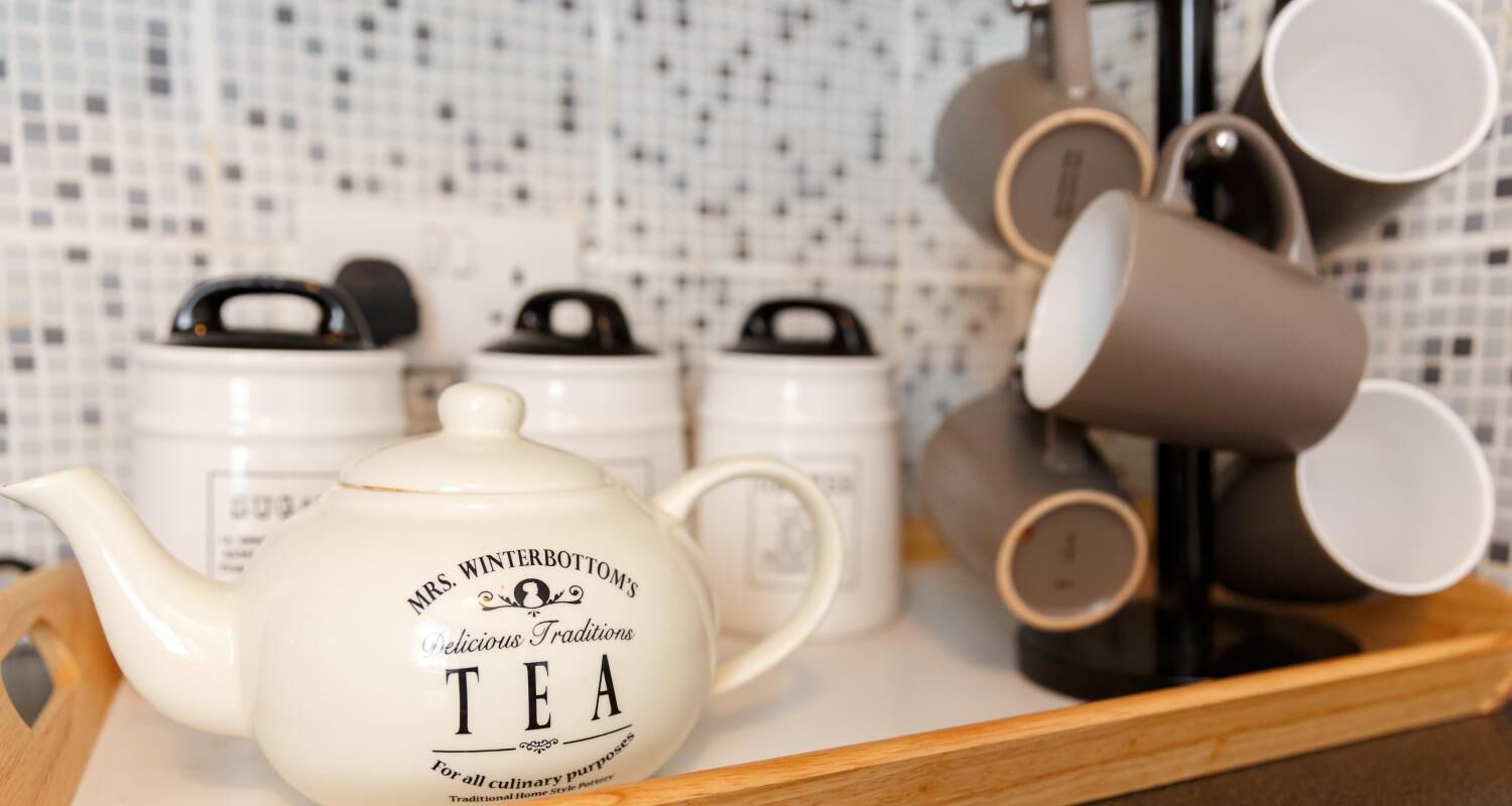 A teapot and several mugs on a tray, with a tiled backsplash in the background.