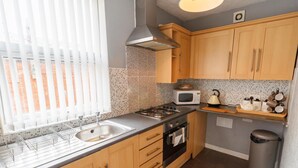 A kitchen with wooden cabinets, a microwave, a kettle, and a sink.