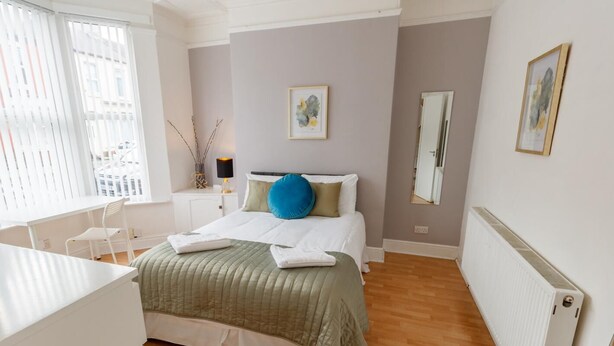 A bedroom with a bed, a desk, and a window with blinds.