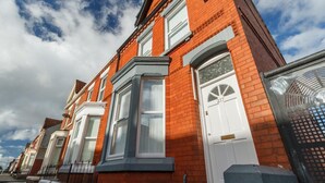 A row of red brick terraced houses with white doors and windows, a clear sky, and a metal fence in the foreground.