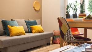 Un salon moderne avec un canapé gris, des coussins jaunes et bleus, une table à manger en bois et une chaise à motifs.