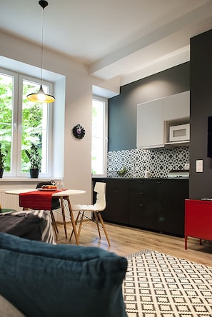A modern kitchen with a dining area, large windows, and a patterned rug.