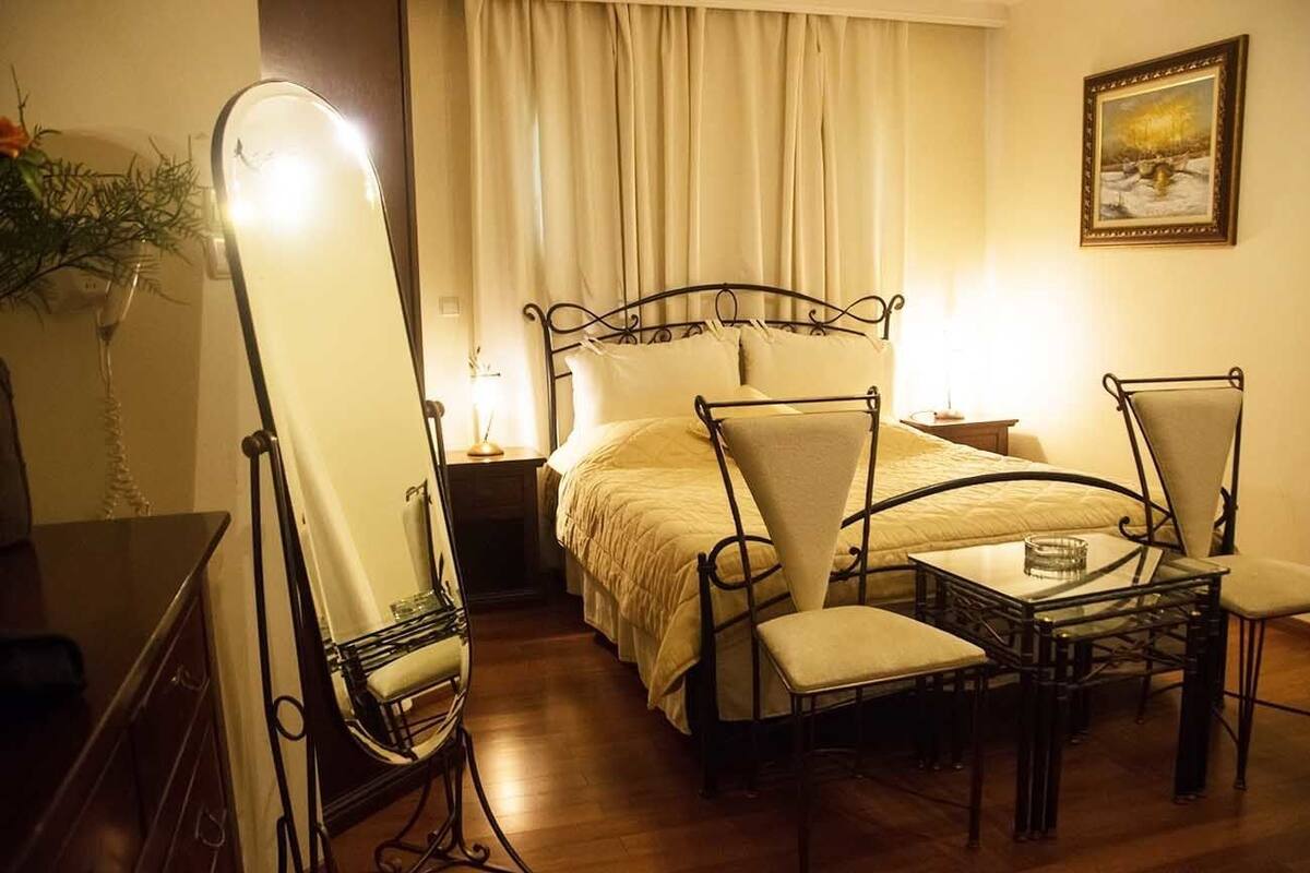A hotel room with a bed, a chair, a table, and a mirror.