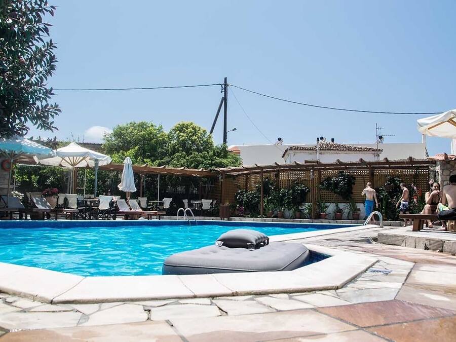Una piscina con sillas de descanso y sombrillas, rodeada por una terraza de piedra y una pérgola de madera.