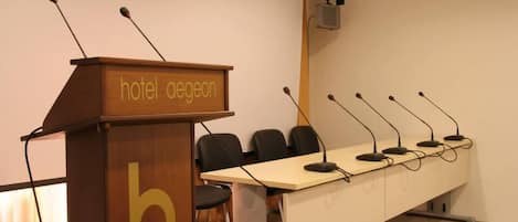 A conference room with a podium labeled "hotel aegeon" and a long table with multiple microphones.