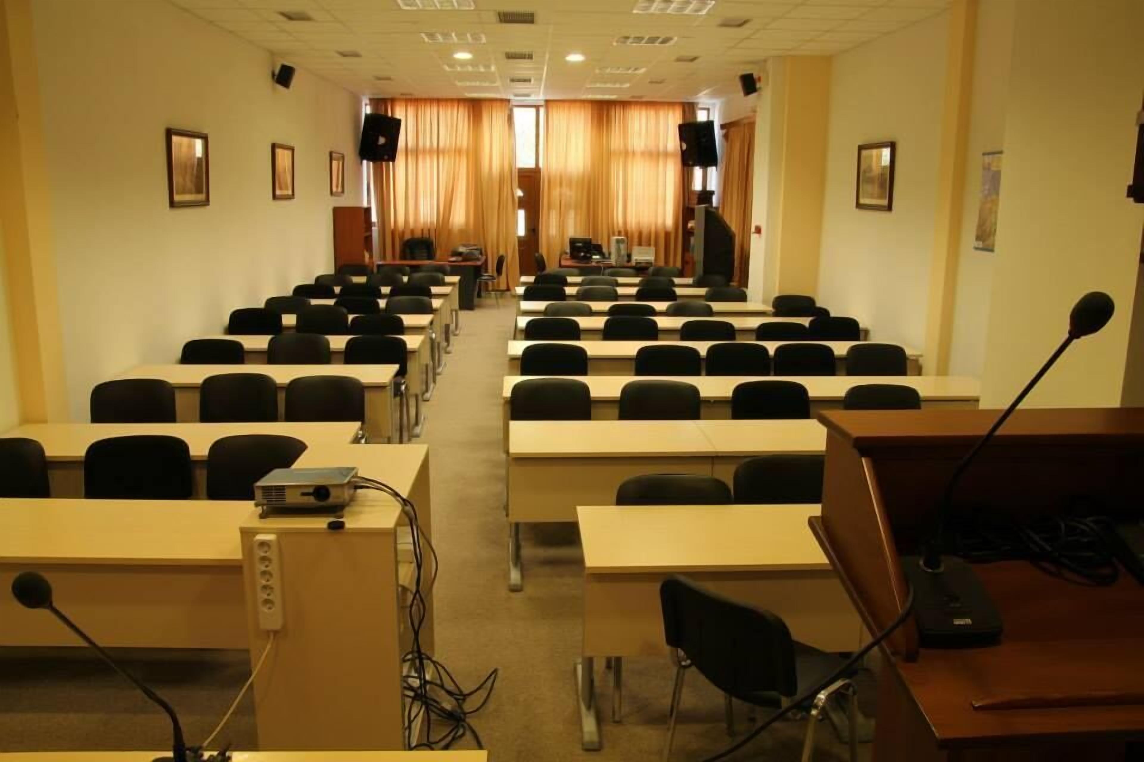 Ein Konferenzraum mit Tischen und Stühlen in Reihen, ausgestattet mit Projektoren und Mikrofonen.
