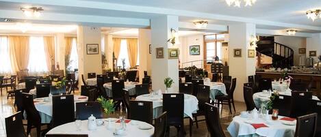 A spacious dining area with round tables, chairs, and chandeliers.
