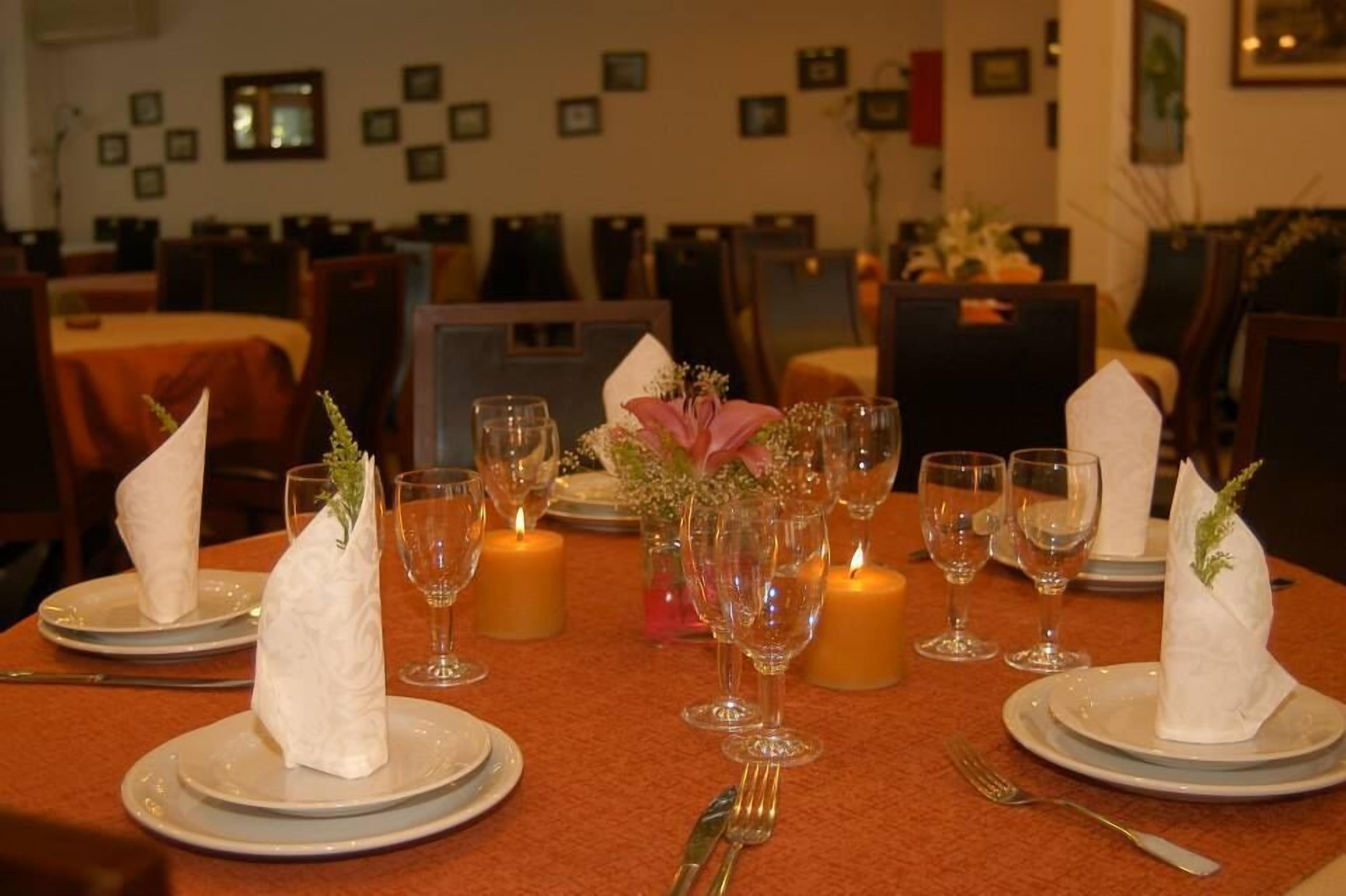 A dining table set with plates, glasses, and candles, surrounded by chairs.