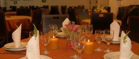 A dining table set with plates, glasses, and candles, surrounded by chairs.