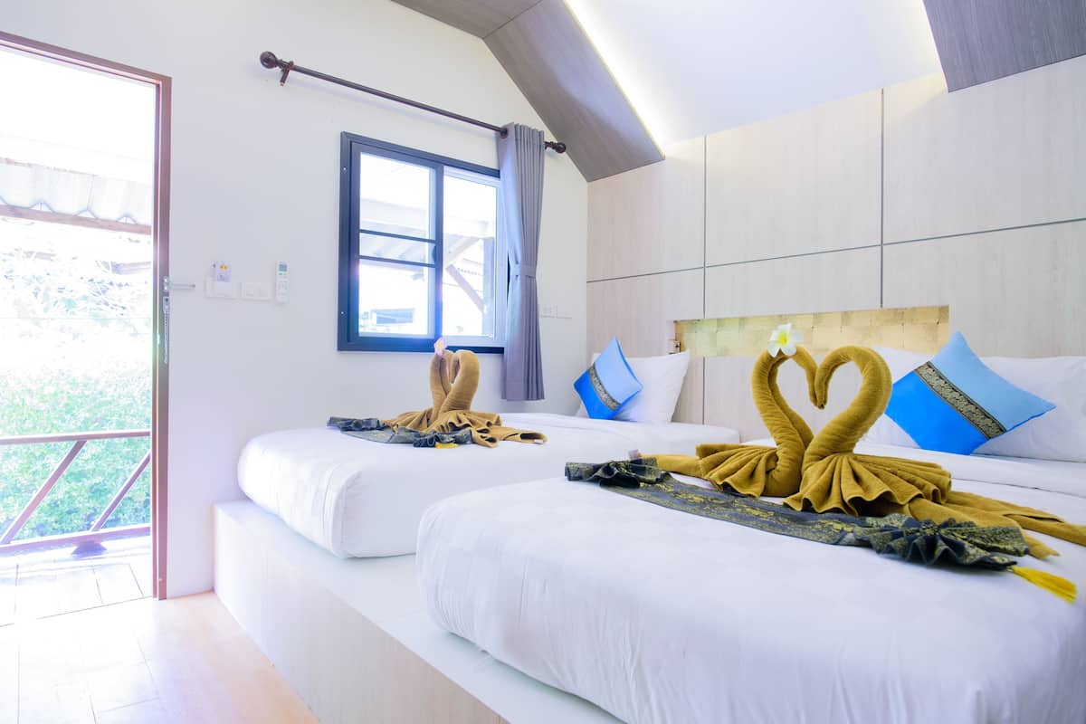 A hotel room with two beds, a window with curtains, and a view of greenery outside.