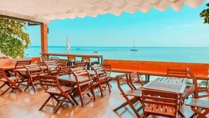 Un espacio al aire libre con mesas y sillas de madera, con vista a un mar tranquilo con barcos.