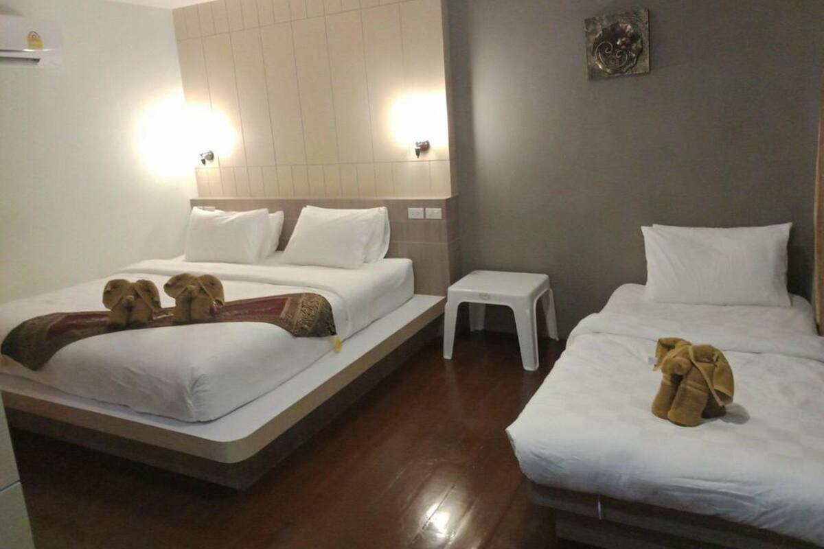 A hotel room with two beds, a small white table, and a wall-mounted light fixture.