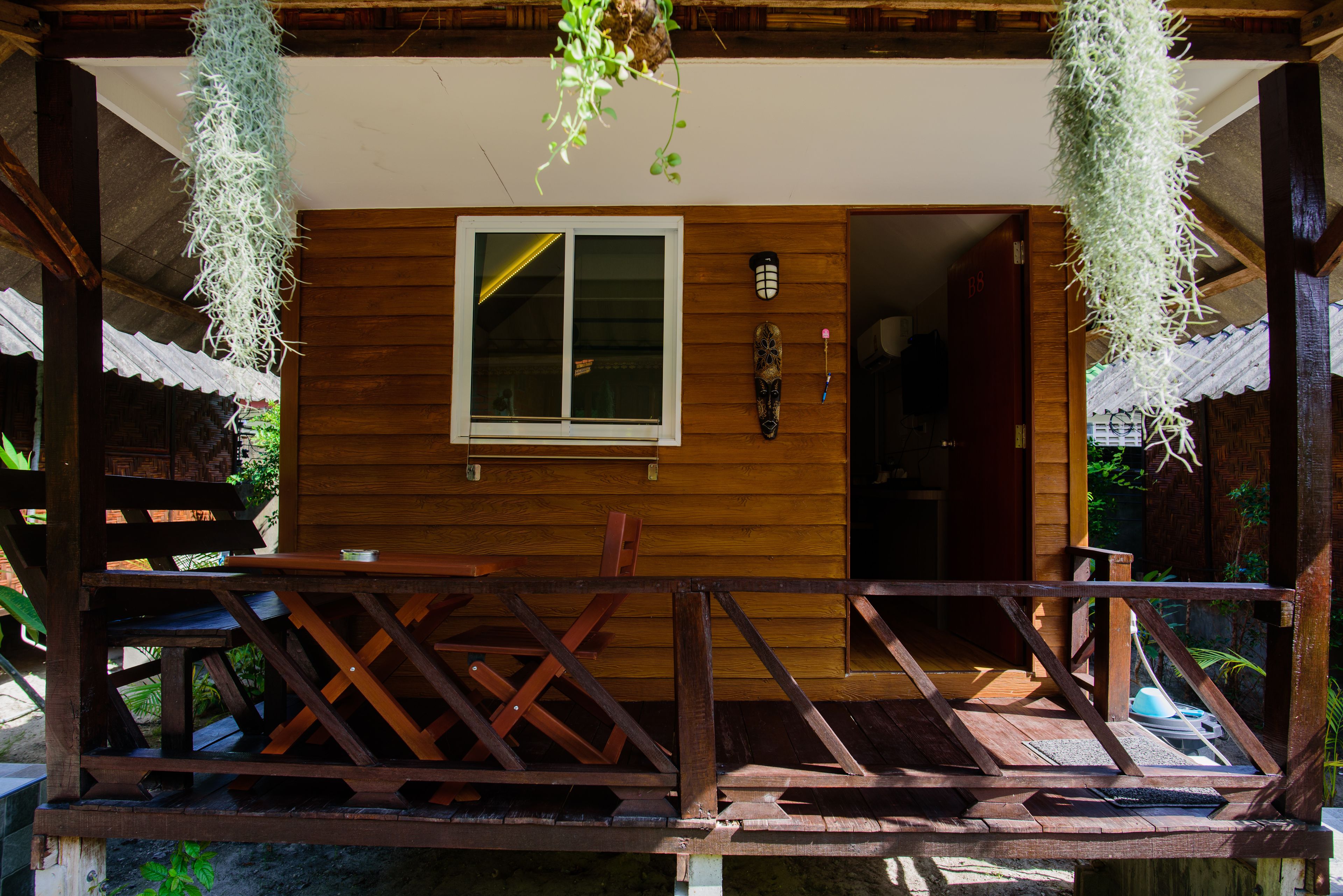 A wooden cabin with a porch, a window, and hanging plants.