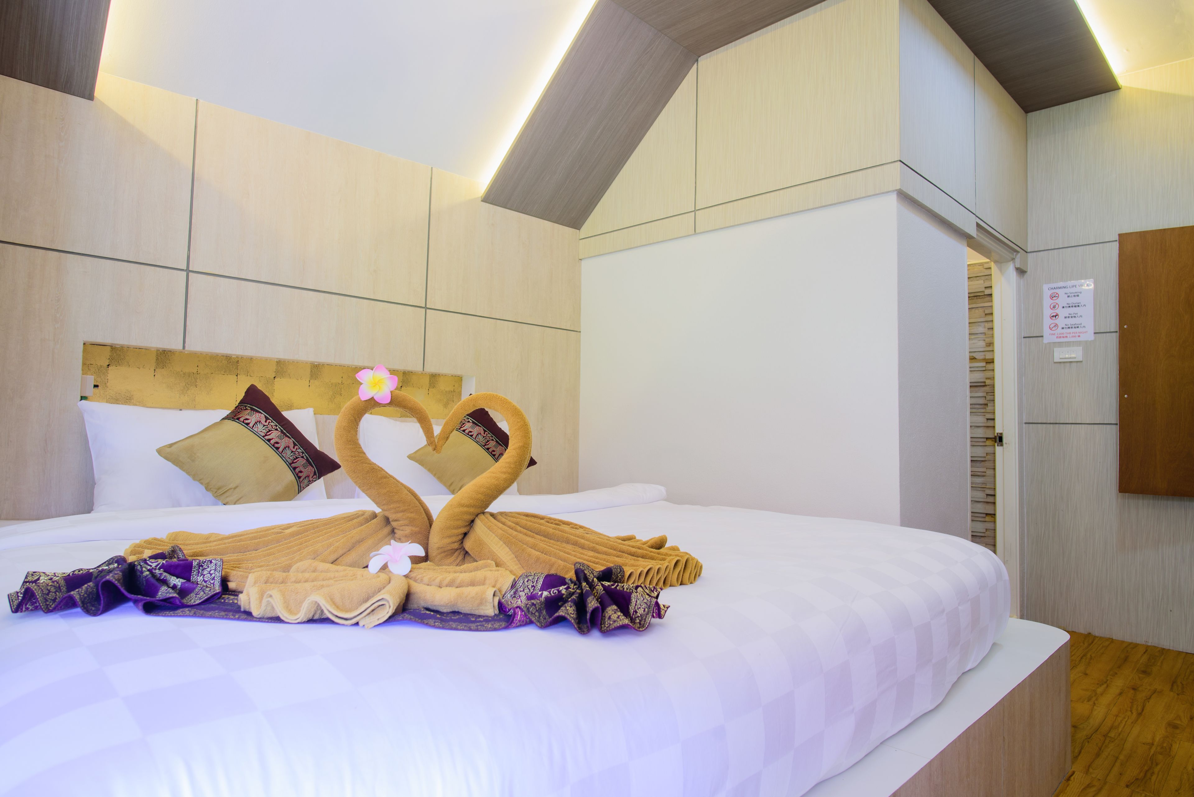 A hotel room with a neatly made bed, a wooden headboard, and a sign on the wall.