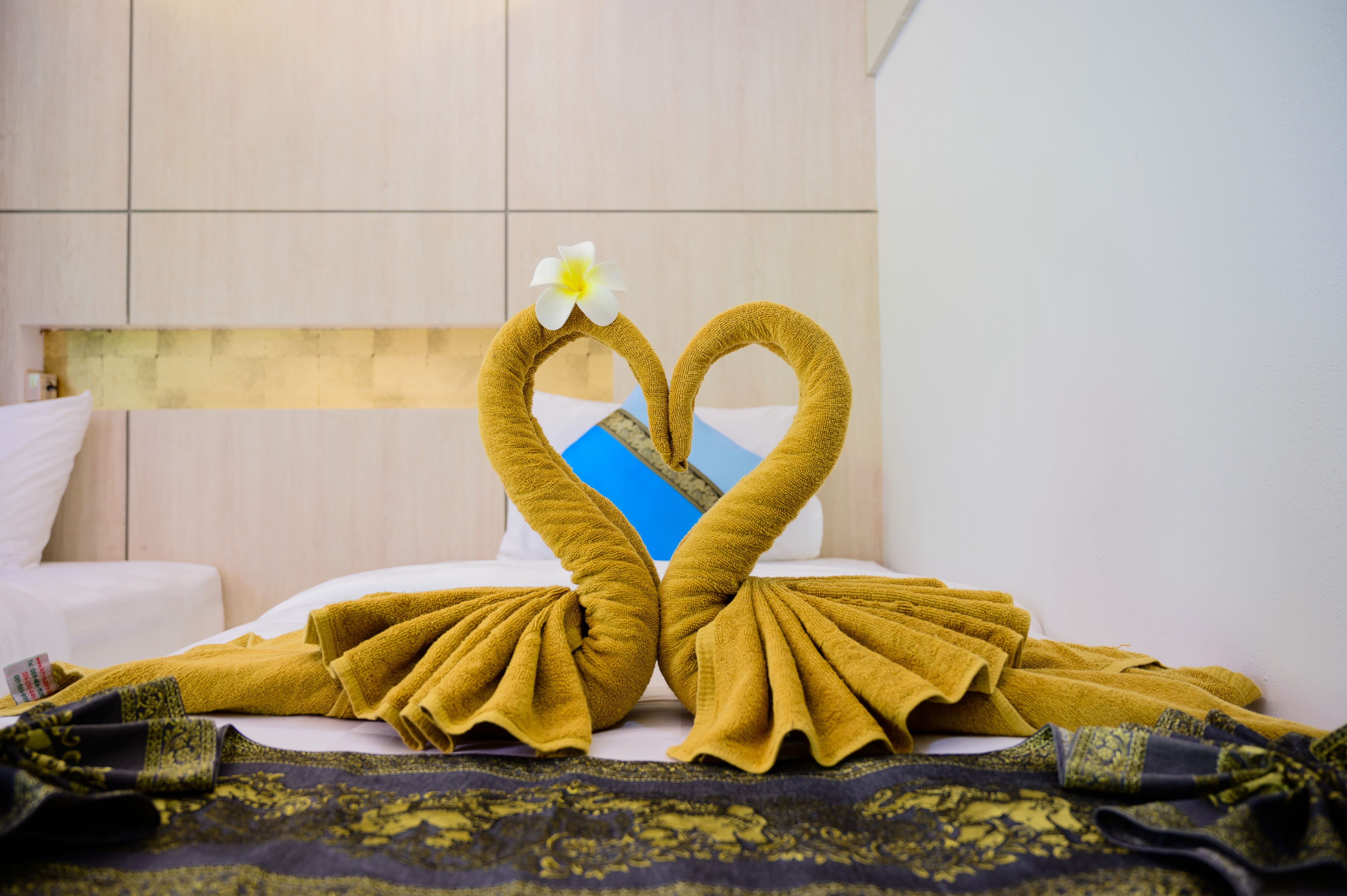A hotel room with a bed, a pillow, a blanket, and a towel arranged in a heart shape with a flower on top.
