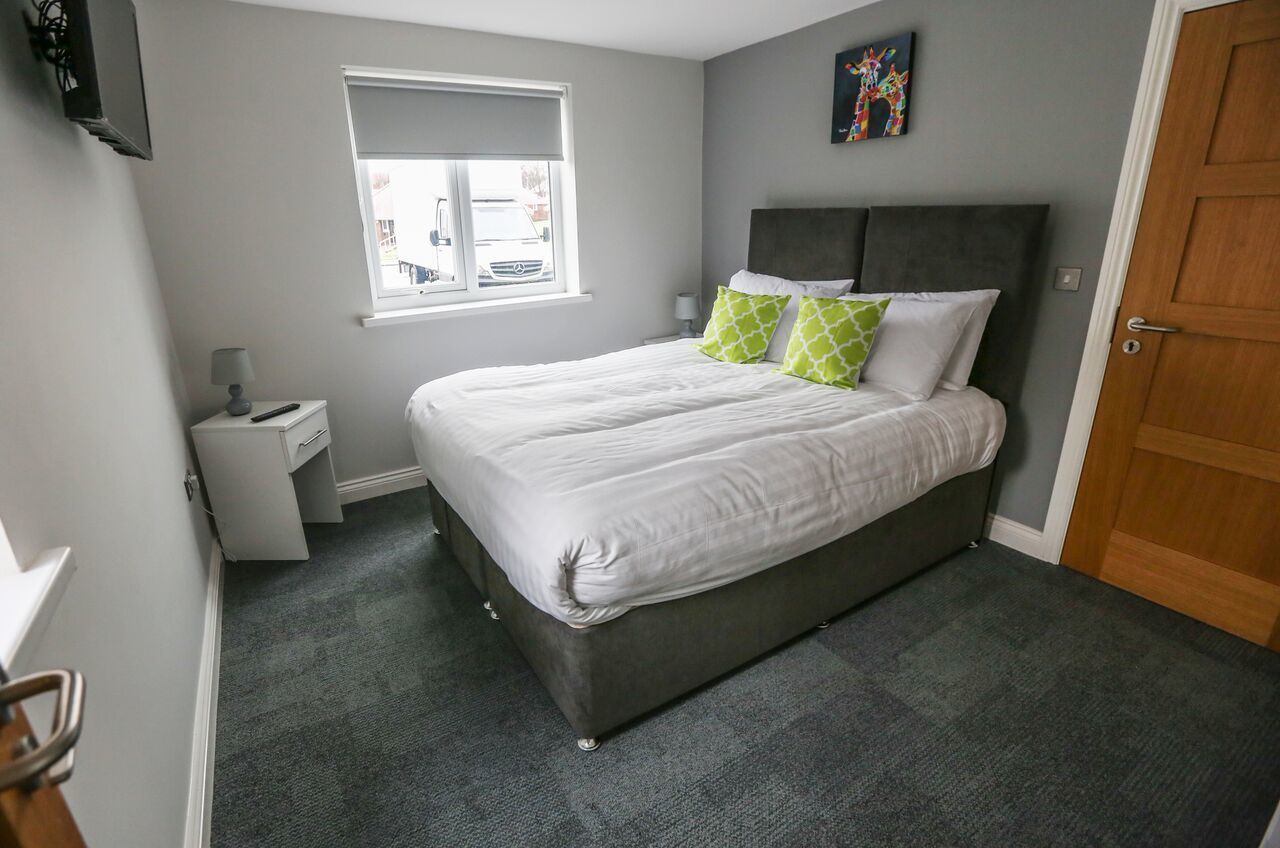 A bedroom with a bed, a nightstand, a window, and a door.