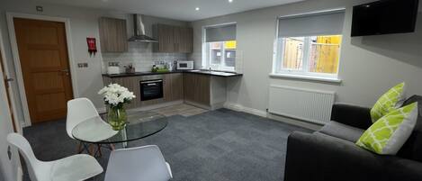 A modern kitchen with a dining area, a sofa, and a TV mounted on the wall.