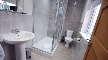 A modern bathroom with a glass-enclosed shower, a pedestal sink, and a toilet.