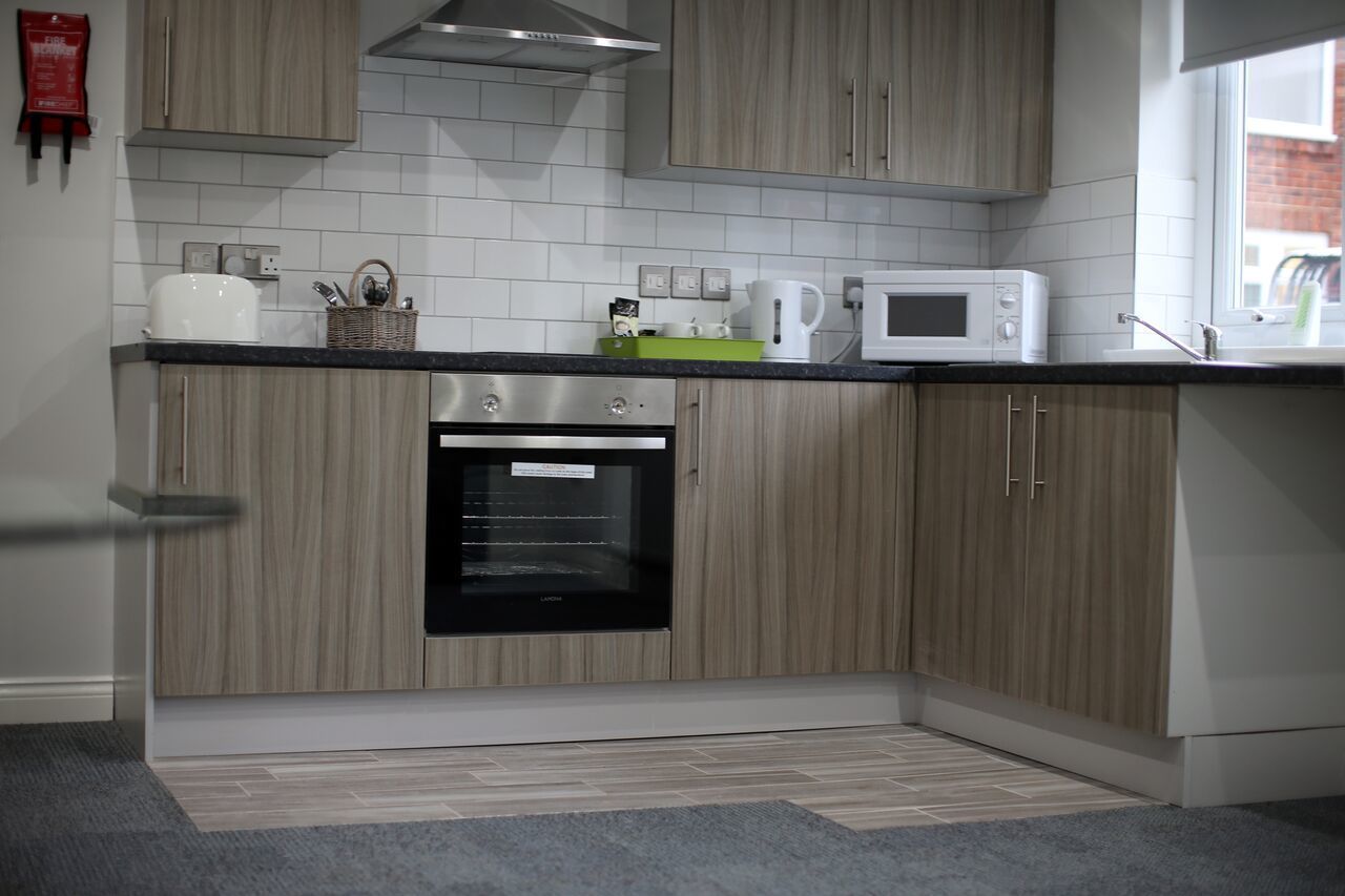 A modern kitchen with light wood cabinets, a built-in oven, a microwave, and a window providing natural light.