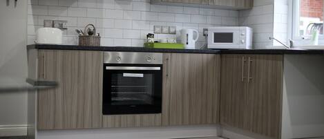 A modern kitchen with light wood cabinets, a built-in oven, a microwave, and a window providing natural light.