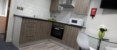 A modern kitchen with wooden cabinets, a microwave, and a glass table with chairs.