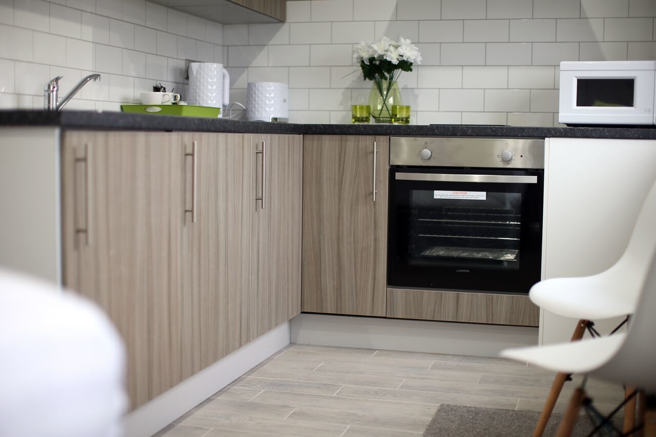 A modern kitchen with light wood cabinets, a built-in oven, and a white microwave on the countertop.