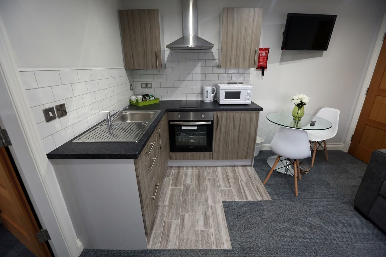 A compact kitchen with a microwave, kettle, and a small dining area with a chair and table.