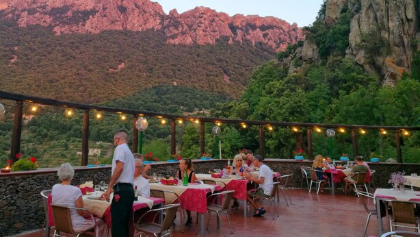 An outdoor dining area with tables and chairs, set against a backdrop of mountains and greenery. - Hotel Sant'Elene (Dorgali)