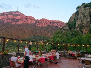 Un área de comedor al aire libre con mesas y sillas, con montañas y vegetación de fondo.