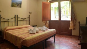 A bedroom with a bed, a wooden cabinet, a window with curtains, and an air conditioning unit. - Hotel Sant'Elene (Dorgali)