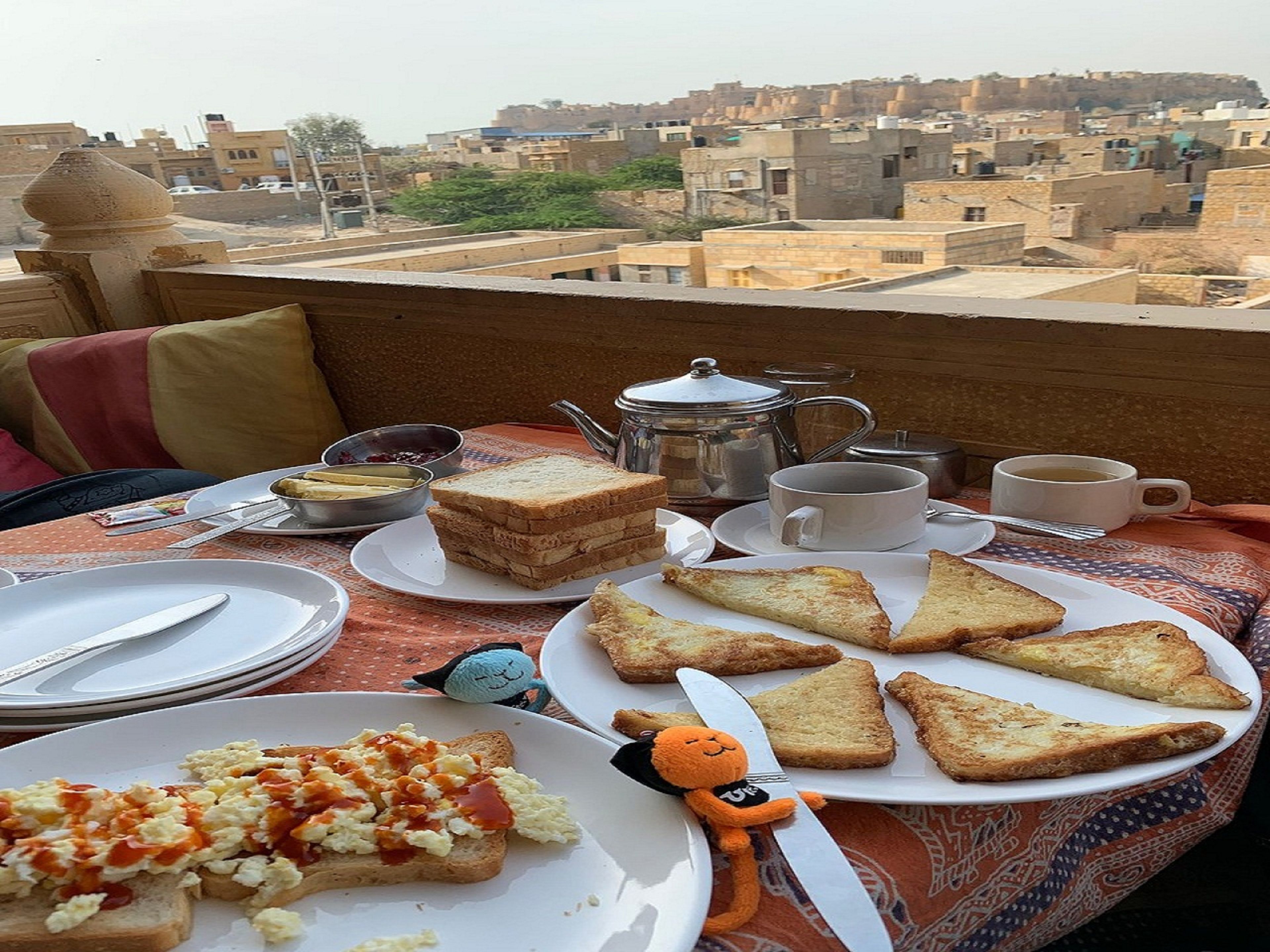 A breakfast setting with toast, scrambled eggs, and tea on a terrace overlooking a cityscape.