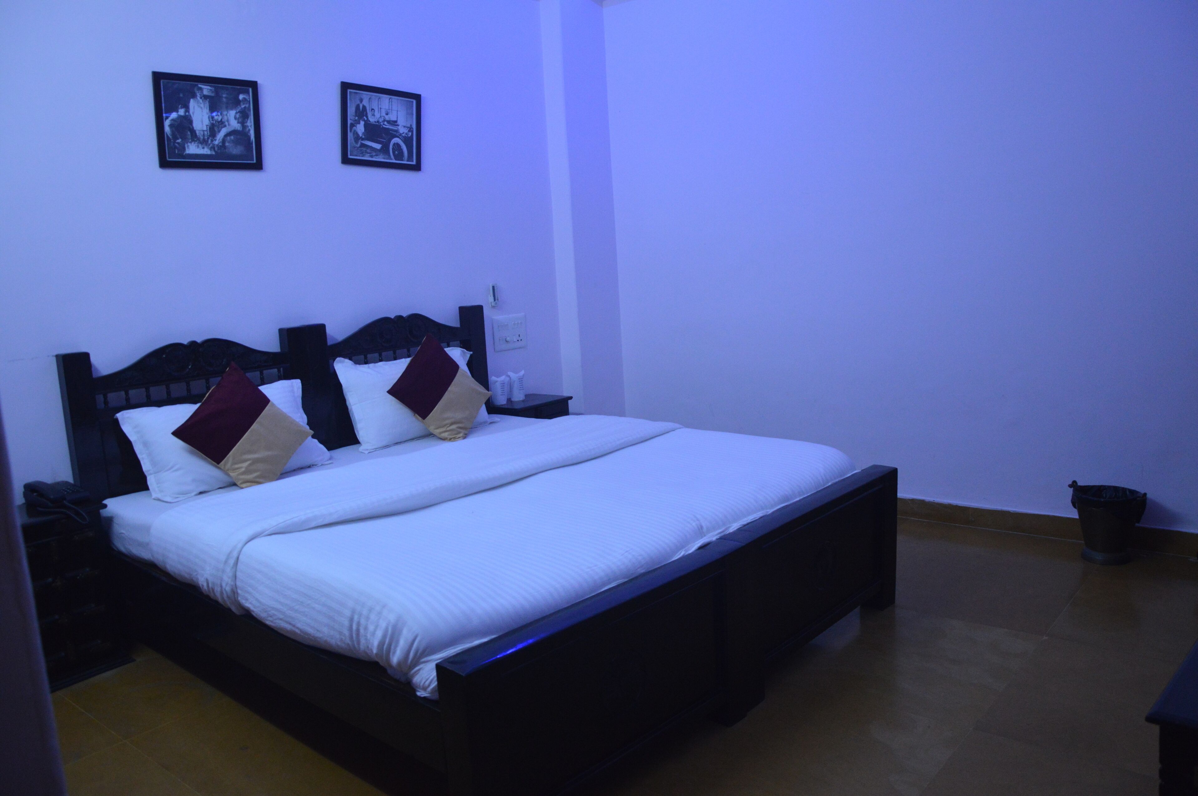 A neatly made bed with white linens and two pillows, a bedside table with a lamp, and two framed pictures on the wall.