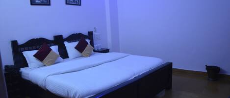 A neatly made bed with white linens and two pillows, a bedside table with a lamp, and two framed pictures on the wall.