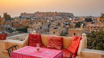 Um terraço com mesa posta para dois, com vista para um horizonte urbano repleto de edifícios históricos e uma fortaleza ao fundo.