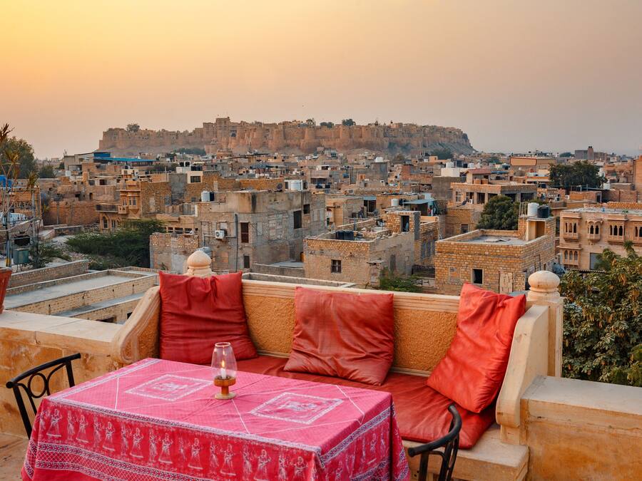 Um terraço com mesa posta para dois, com vista para um horizonte urbano repleto de edifícios históricos e uma fortaleza ao fundo.