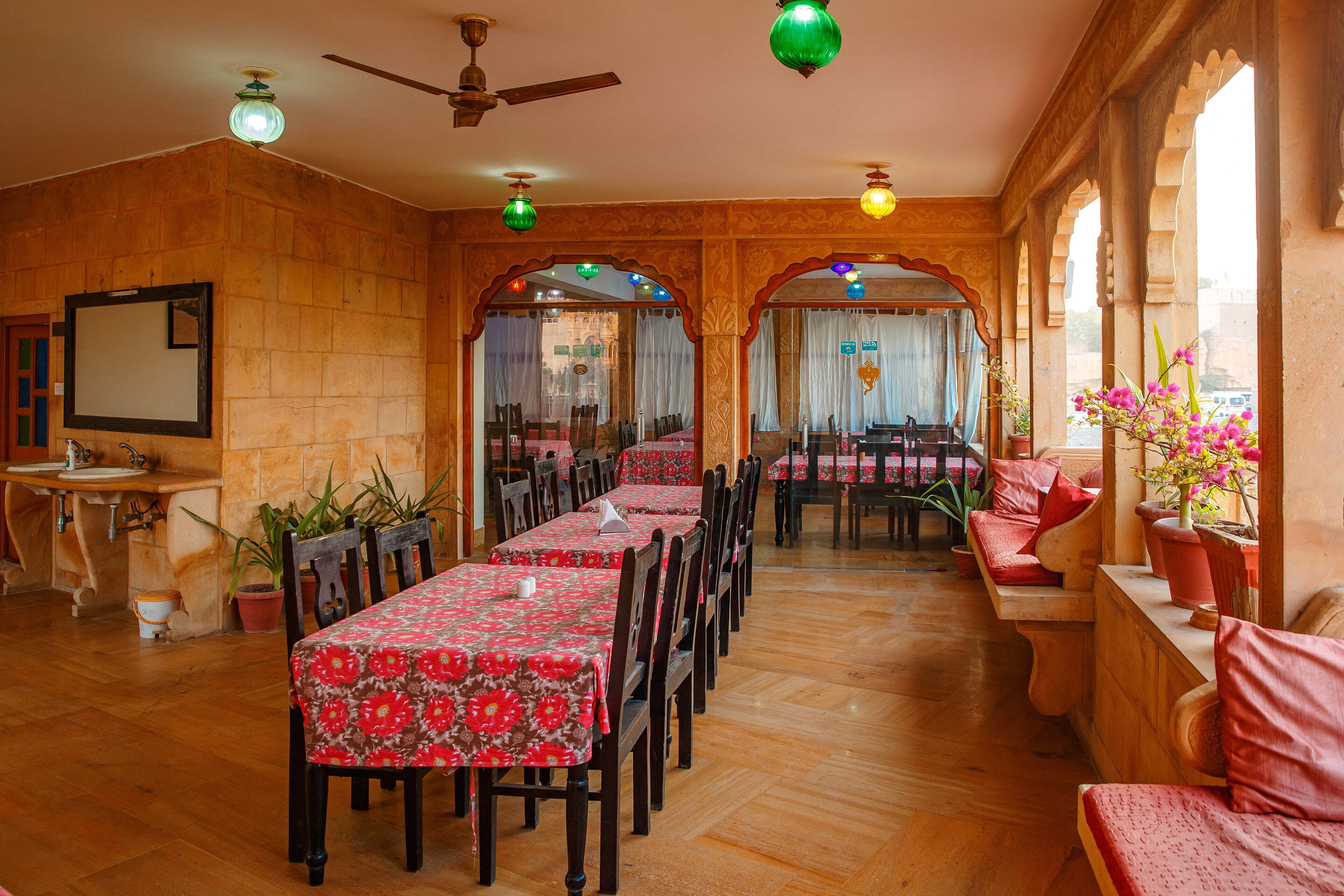 A dining area with wooden walls and arches, tables with floral tablecloths, and potted plants.