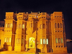 Un grand bâtiment imposant, orné de nombreuses arcades et doté d’une entrée centrale, illuminé la nuit.
